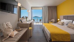 Une chambre d’hôtel équipée d’un lit, d’un bureau, d’une chaise, d’un canapé, d’une télévision et offrant une vue sur la mer.