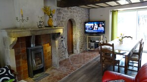 Ein Wohnzimmer mit Kamin aus Stein, einem Fernseher und einem Essbereich mit einem roten Sofa.