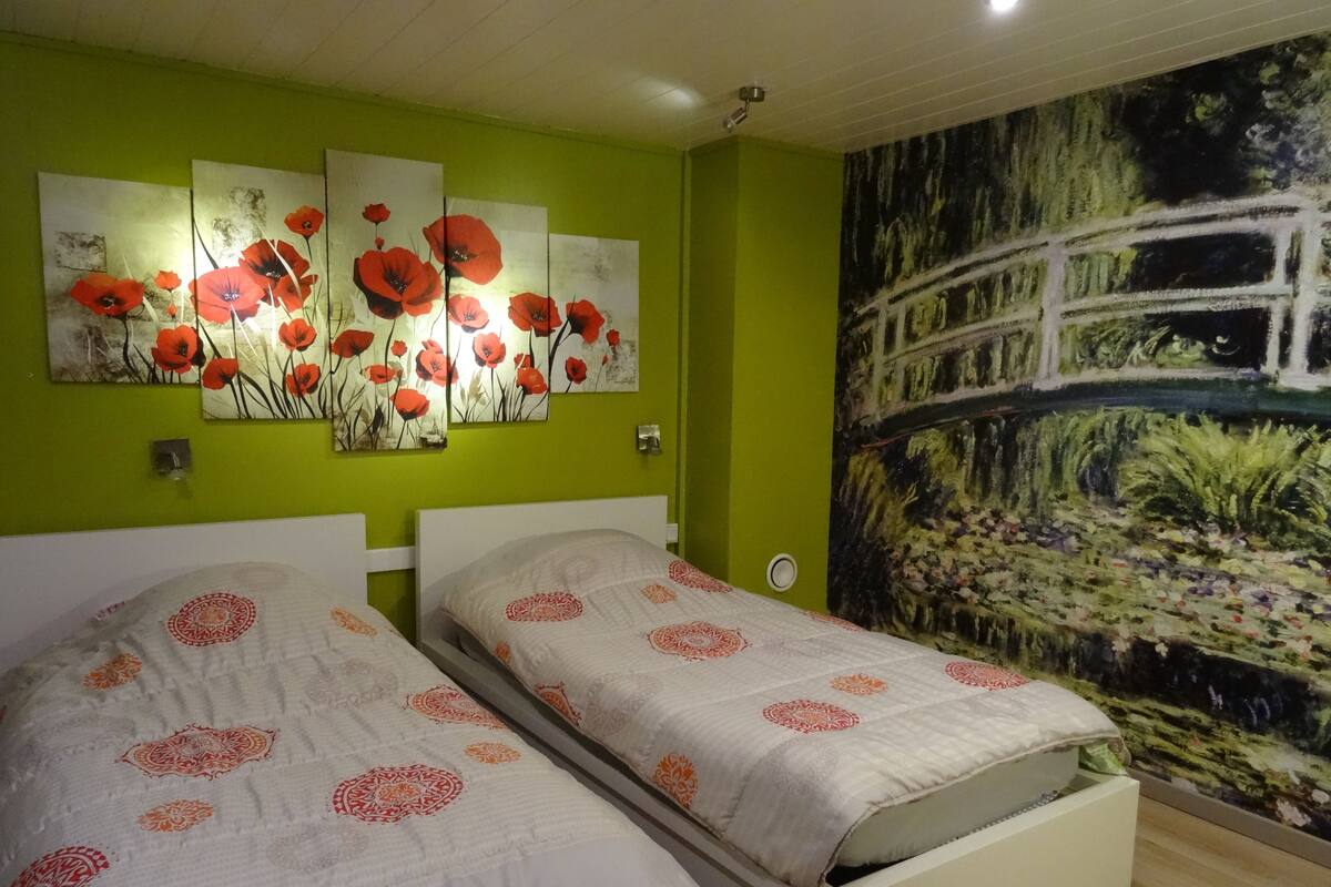 A bedroom with two beds, green walls, and a large mural.