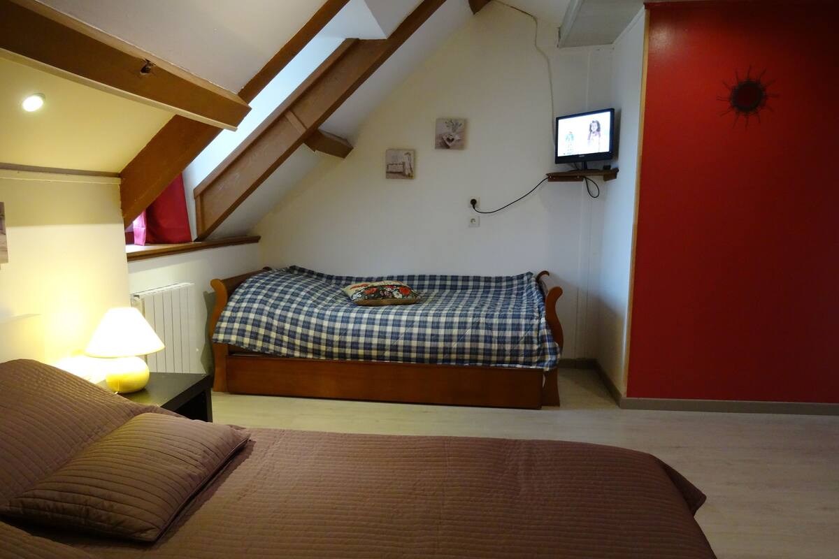 A bedroom with a bed, a TV mounted on the wall, and a red accent wall.