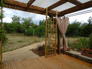 A wooden pergola with a metal gate, a wooden deck, and potted plants.
