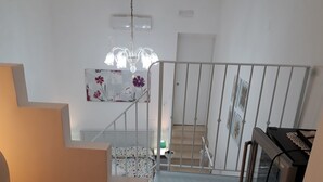 Un escalier avec une rampe blanche, un lustre et un lit recouvert d’une couvre-lit à motifs floraux.