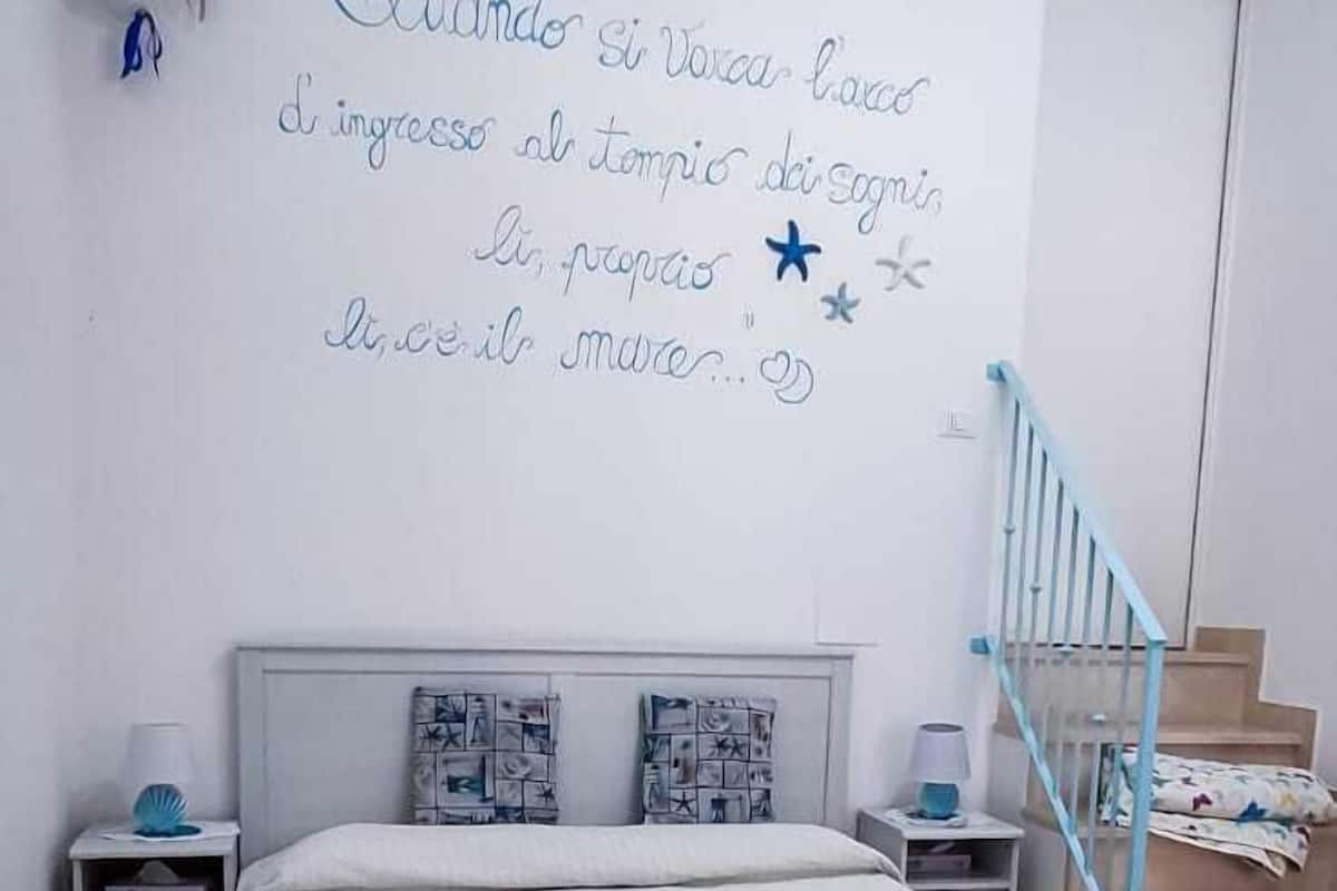 Une chambre à coucher avec un lit, un mur orné d’une inscription décorative, une table de chevet, une lampe et un escalier.