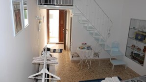 Une pièce avec un escalier, une table entourée de chaises, un fauteuil suspendu et une étagère ornée d’objets décoratifs.