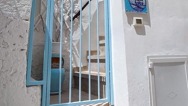 Un bâtiment blanc avec une porte bleue, une petite fenêtre et une enseigne sur fond bleu.