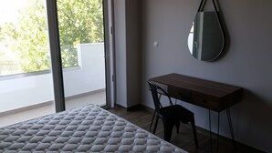 Une chambre à coucher avec un lit, un bureau et une chaise. Il y a une fenêtre donnant sur des arbres et un mur blanc.