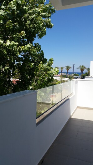 Ein Balkon mit Glasgeländer, der auf einen wolkenlosen, blauen Himmel und eine entfernte Ansicht von Palmen und Gebäuden blickt.