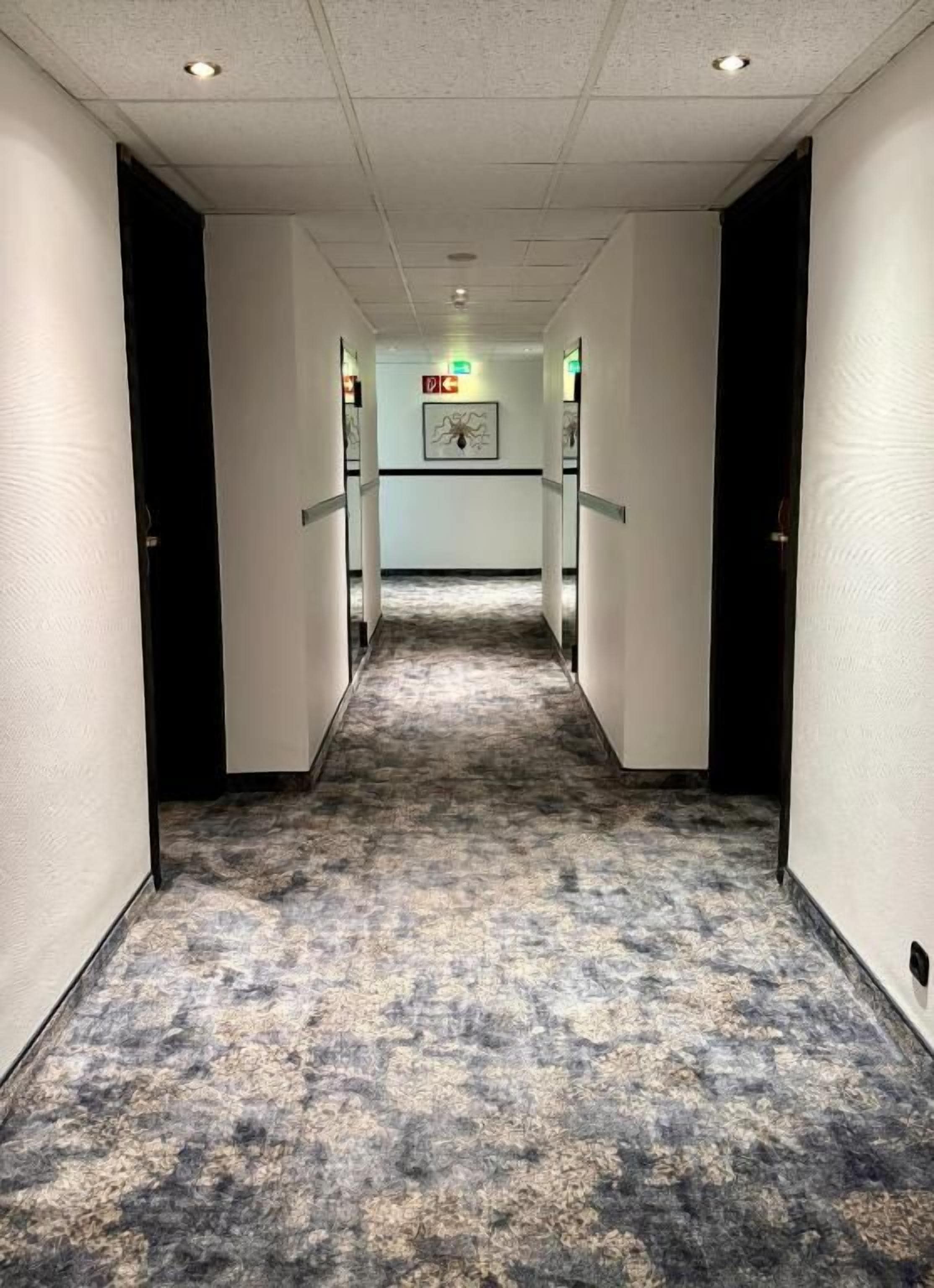 Ein Hotelgang mit Teppichboden, weißen Wänden und Türen auf beiden Seiten.