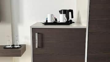 Een donkere houten kast met een koffiezetapparaat en kopjes bovenop, een klein plankje met glazen, en een spiegel aan de linkerkant.