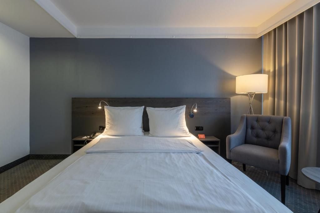 Una habitación de hotel con una cama grande, una mesita de noche, una lámpara y una silla.