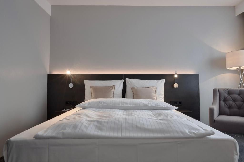 A hotel room with a bed, bedside lamps, a chair, and a nightstand.