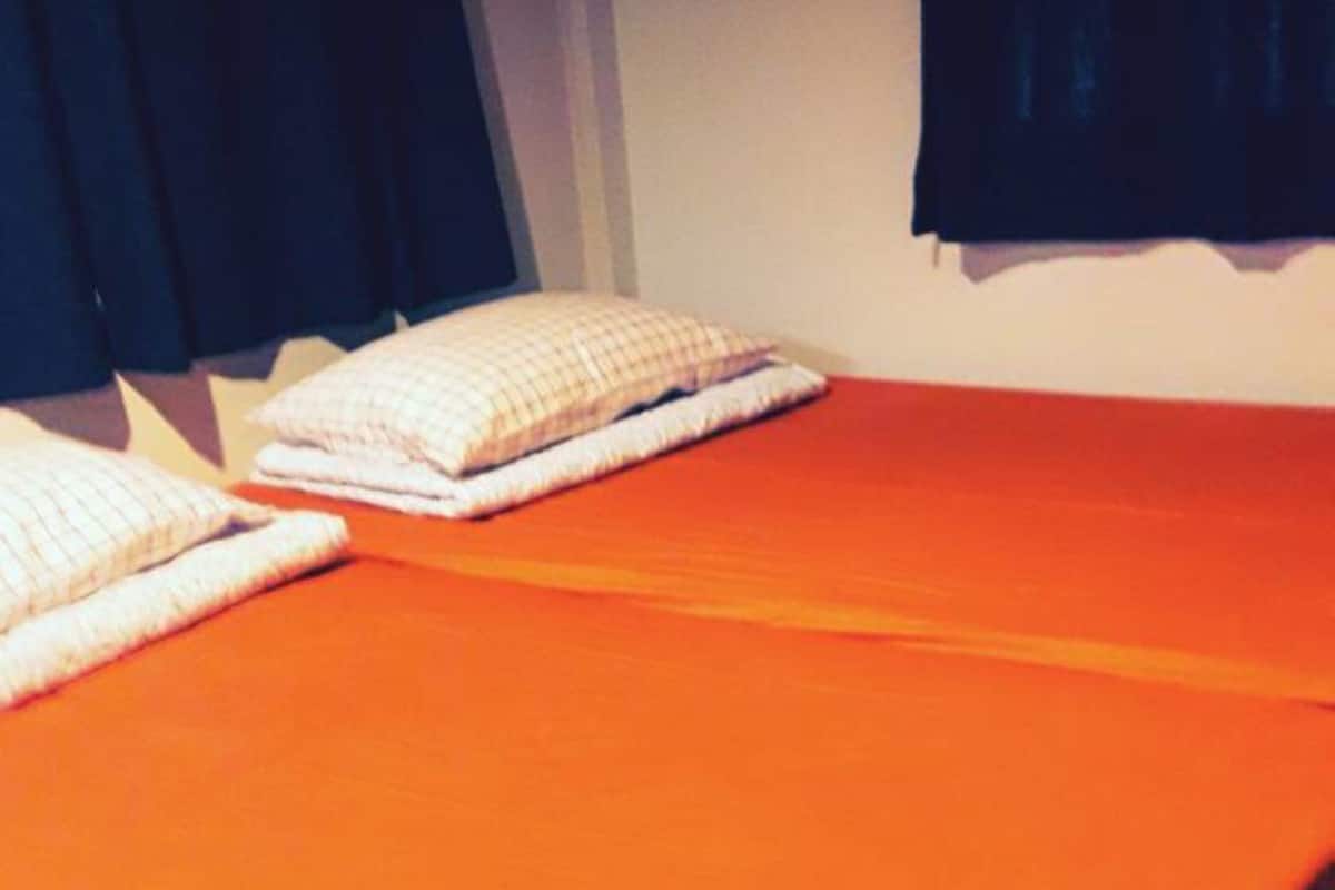 A single bed with an orange bedspread and two pillows.