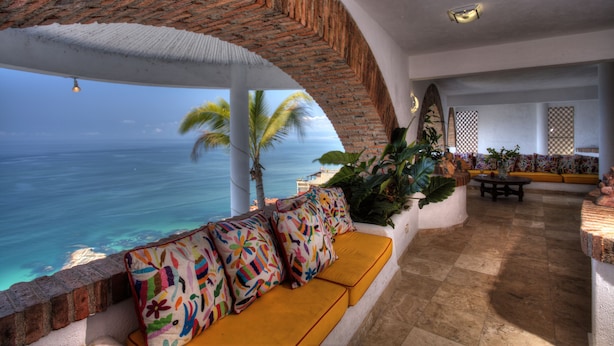 Una habitación con vista al océano, un arco de ladrillo, un sofá con cojines de colores, una mesa y un papel tapiz estampado.