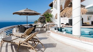 Un área junto a la piscina con sillones, una mesa y una sombrilla.