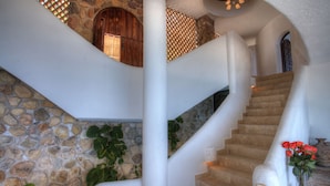 Una escalera de piedra con barandilla blanca, una puerta de madera y un florero con flores rojas.