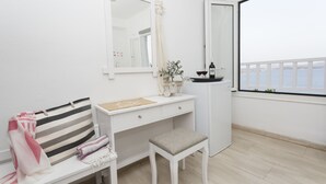 A white room with a bench, a small table, a mirror, and a window with a view of the sea. - Galini Mare (Agios Vasileios)