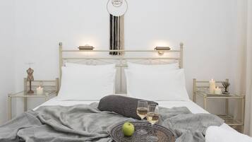 A neatly made bed with white linens, a gray blanket, and a tray with a green apple and two glasses of wine.