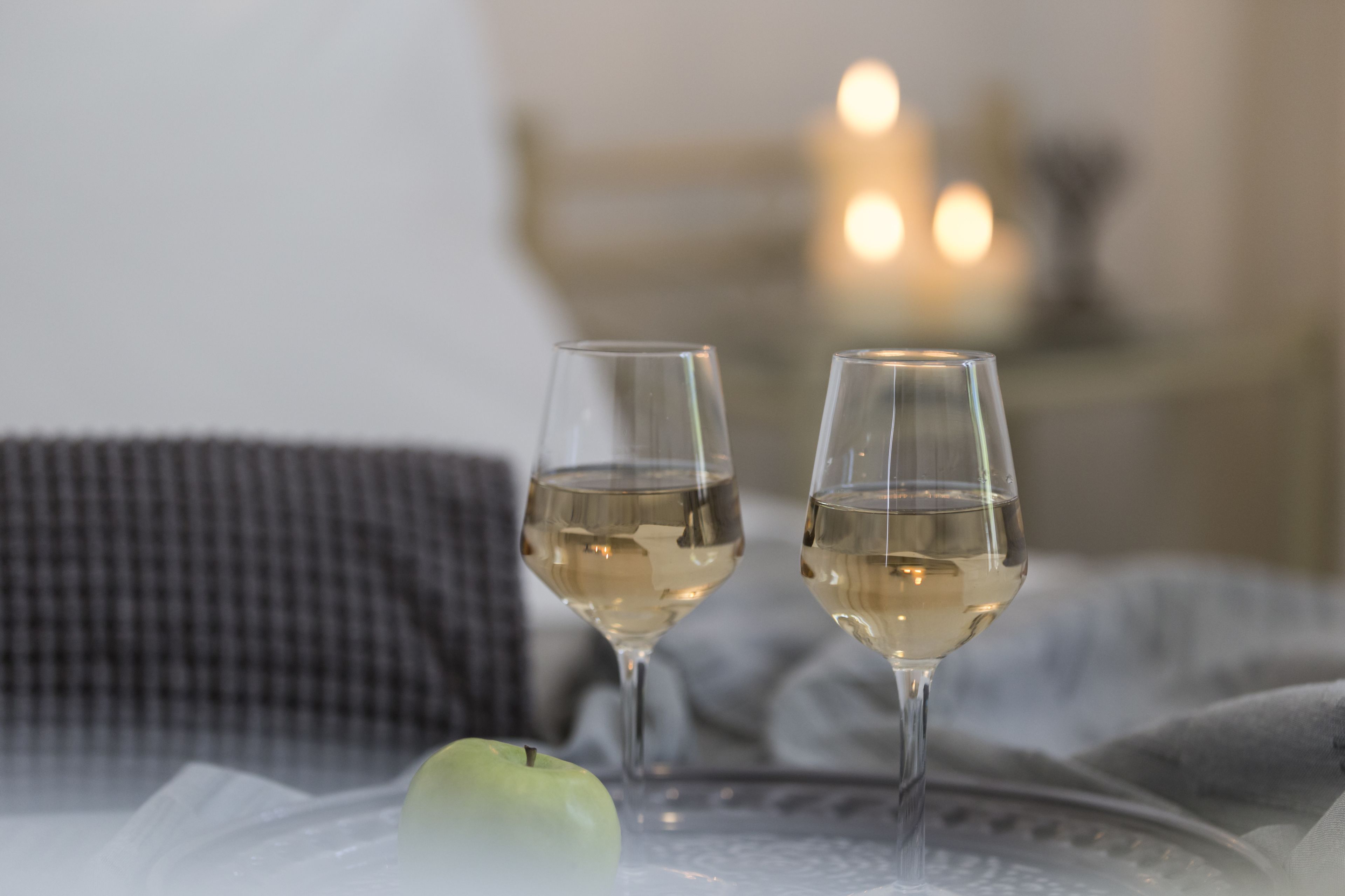 Two glasses of white wine on a table with a green apple beside them.