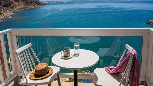 A balcony with a table, two chairs, a straw hat, a glass, and a pink towel. - Galini Mare (Agios Vasileios)