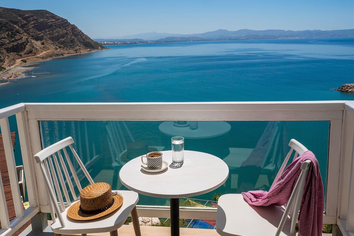 A balcony with a table, two chairs, a straw hat, a glass, and a pink towel.
