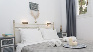 A neatly made bed with white linens, a bedside table with a lamp, and a wall-mounted macrame decoration. - Galini Mare (Agios Vasileios)