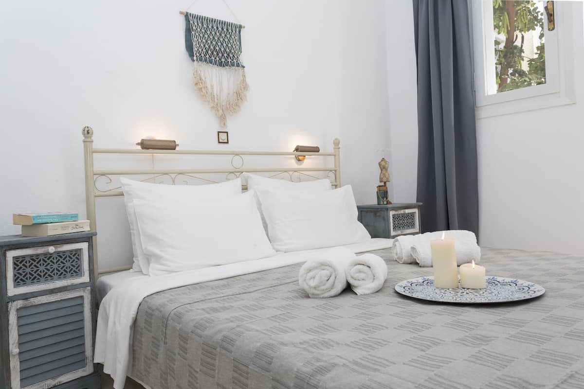 A neatly made bed with white linens, a bedside table with a lamp, and a decorative macrame wall hanging.