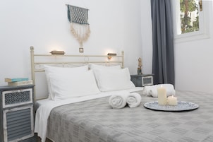 Un lit bien fait, avec du linge de lit blanc, une table de chevet avec une lampe et une décoration en macramé accrochée au mur.