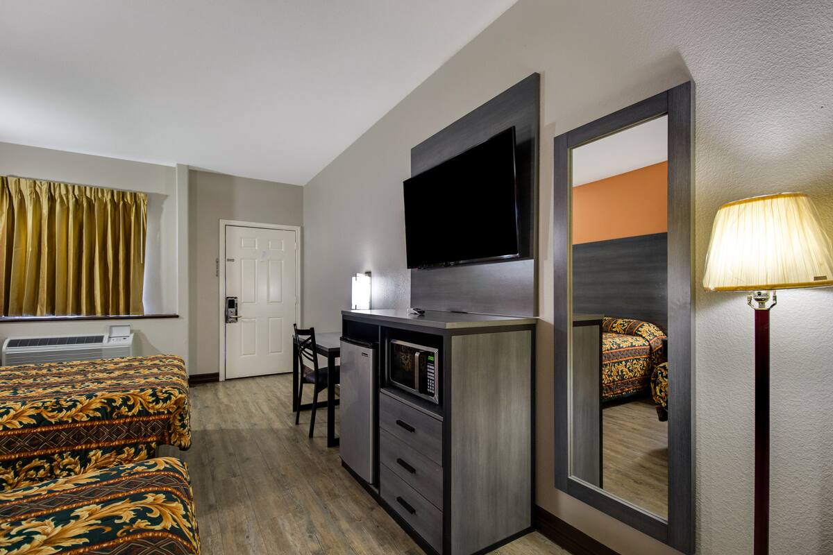 A hotel room with a bed, a desk with a television, a microwave, and a chair.