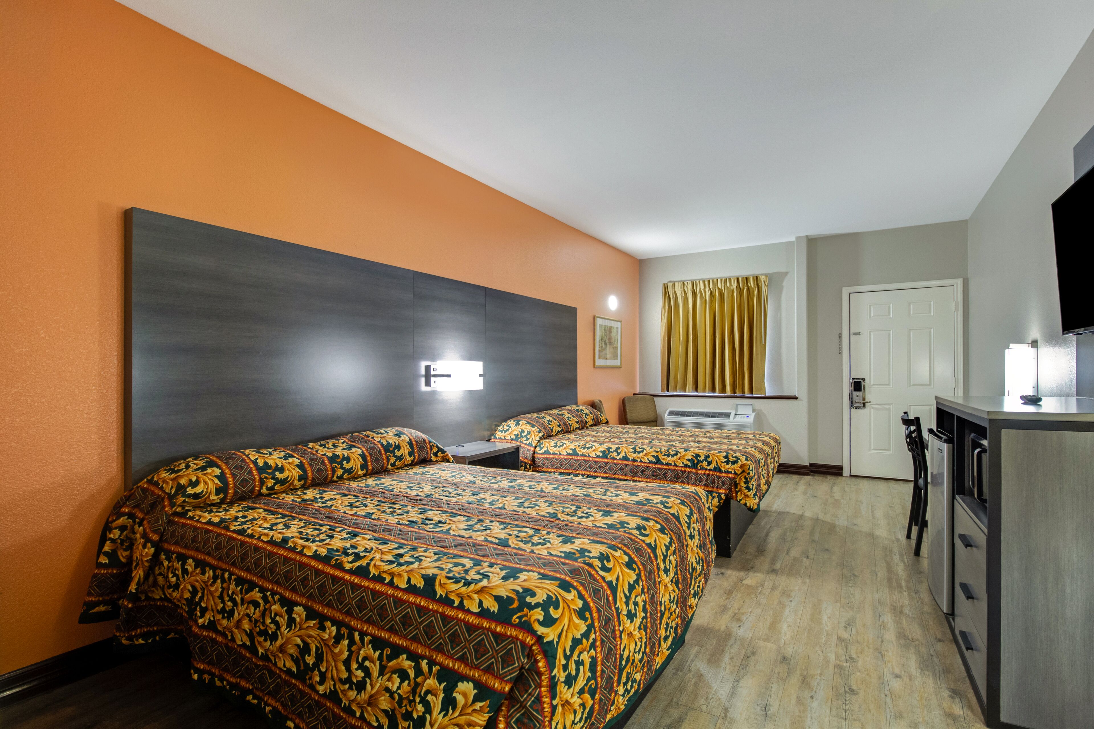 A hotel room with two beds, a desk, a TV, and a kitchenette.