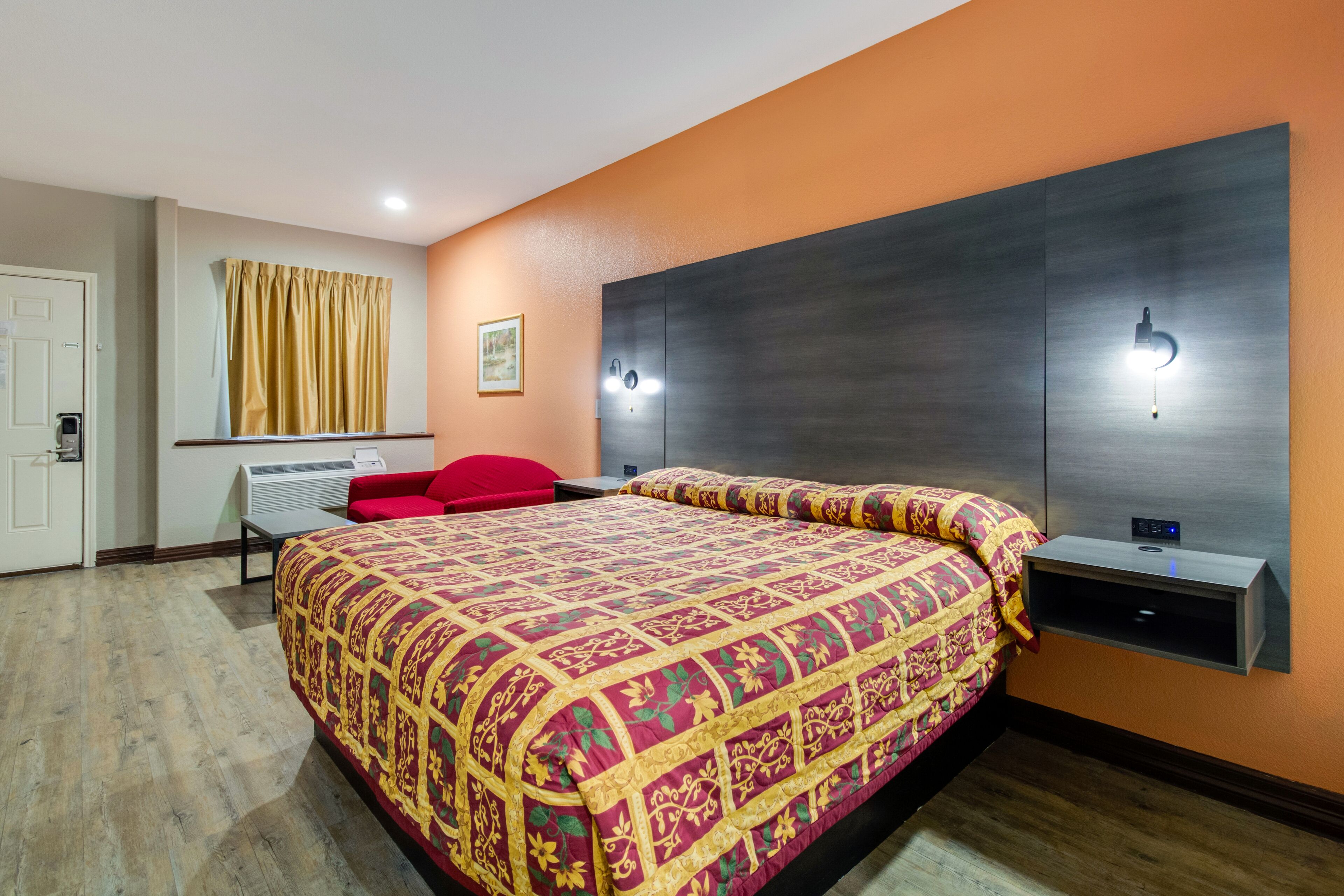 A hotel room with a large bed, a red chair, a desk, and a window with curtains.