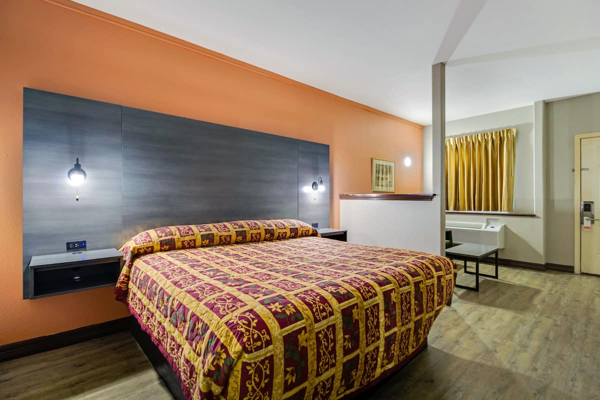 A hotel room with a large bed, a bedside table, a desk, and a mirror.