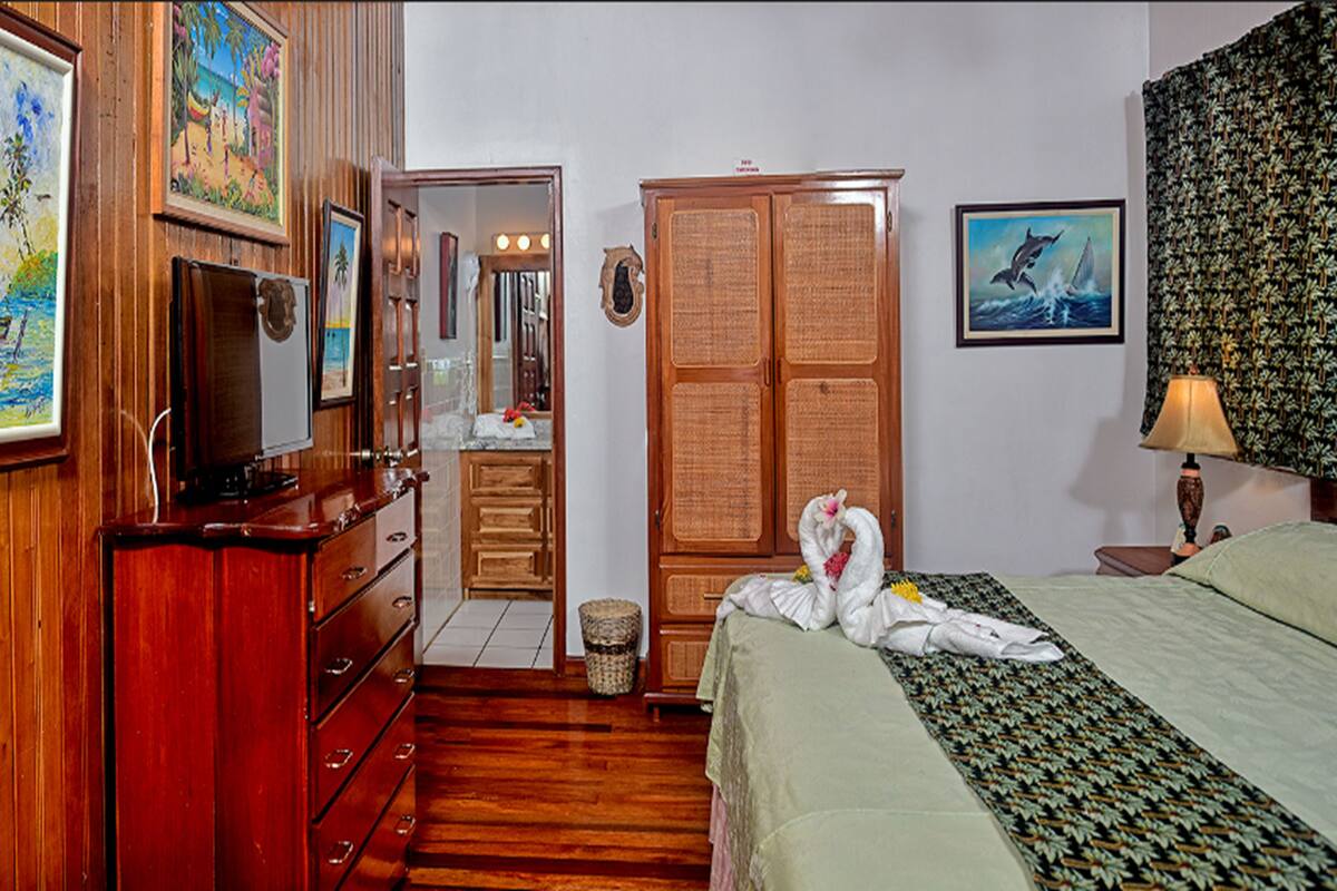 Quarto de hotel com painéis de madeira, cama com colcha estampada, guarda-roupa, espelho e obras de arte nas paredes.