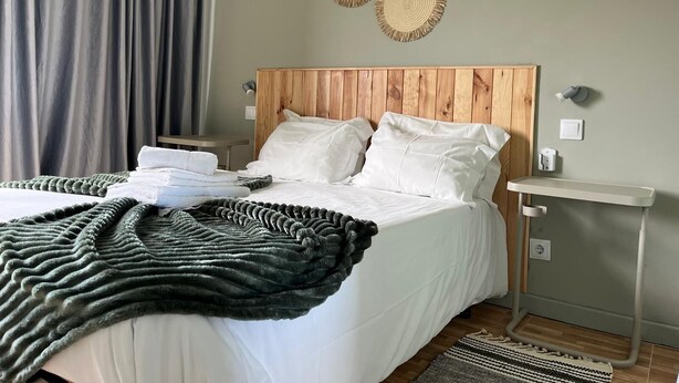 A neatly made bed with white linens, a wooden headboard, and a bedside table with a lamp.
