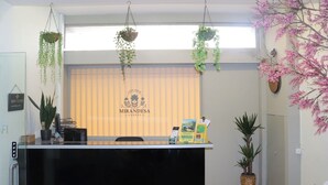 A reception desk with hanging plants, a sign reading "Mirandesa Garden", and a window with blinds.