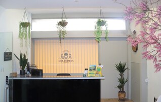 Una recepción con plantas colgantes, un cartel que dice "Mirandesa Garden" y una ventana con persianas.