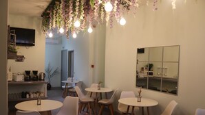 A modern cafe with round tables and chairs, a flat-screen TV, and a decorative ceiling with hanging lights and flowers.