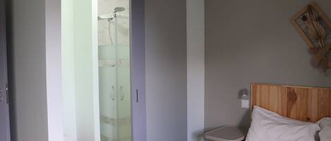 A bedroom with a bed, a bedside table, a wooden headboard, a shower with a glass door, and a toilet.