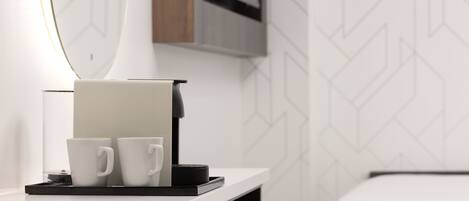 Une chambre d’hôtel moderne avec un lit blanc, une table de chevet sur laquelle se trouve une machine à café, et deux tasses blanches.