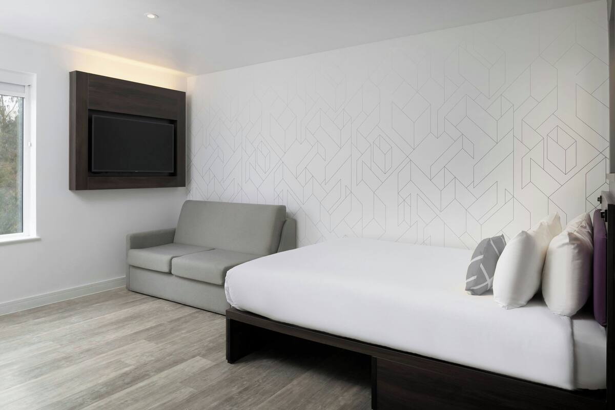 Un dormitorio moderno con cama, sofá, televisor montado en la pared y un diseño geométrico en la pared.