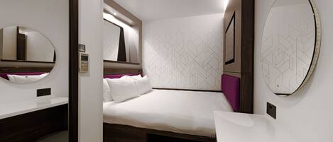 Una habitación de hotel moderna con una cama bien hecha, una mesita de noche, una silla y un espejo grande.