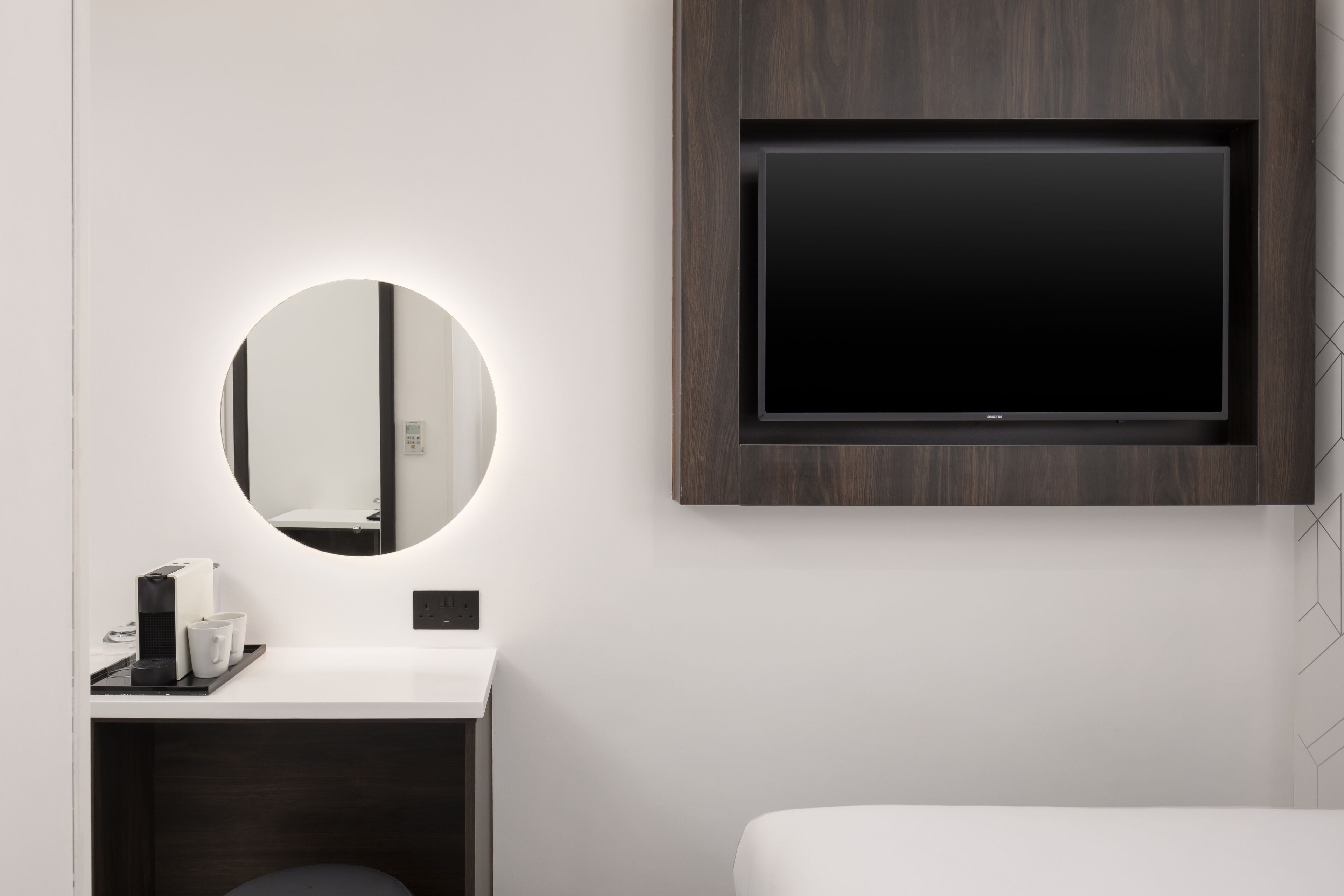 Une salle de bain moderne avec un miroir rond, un téléviseur à écran plat et un lavabo blanc.