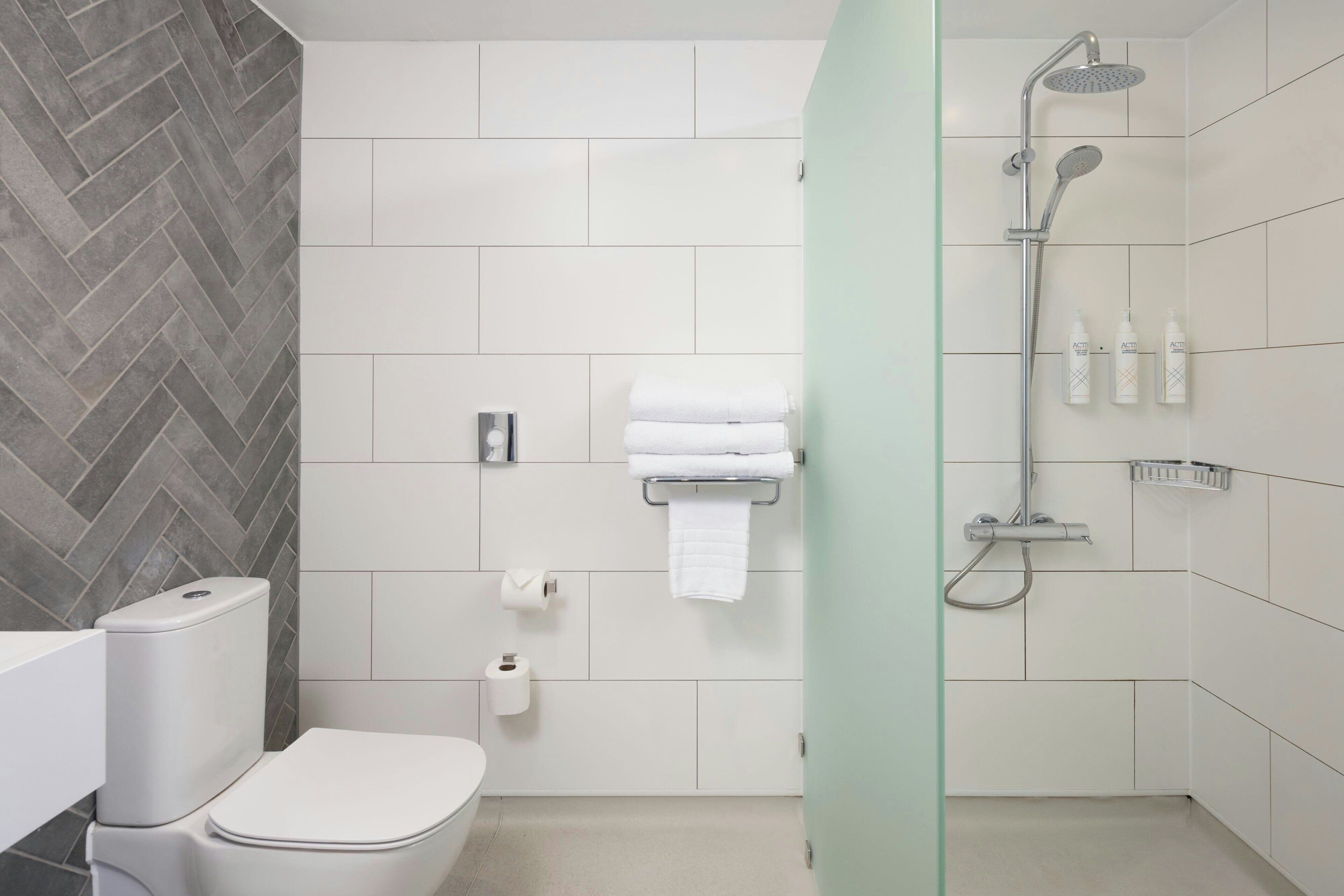 Une salle de bain moderne équipée de toilettes, d’une douche et d’une paroi en verre.