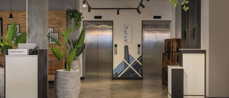 Un intérieur comprenant deux ascenseurs, un comptoir d’accueil et une grande plante en pot.