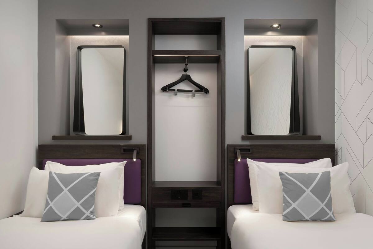 Habitación de hotel con dos camas, un espejo central y un perchero.
