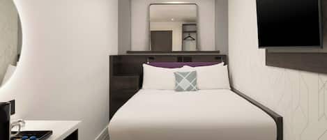 A modern hotel room with a neatly made bed, a flat-screen TV mounted on the wall, and a small desk with a coffee maker.