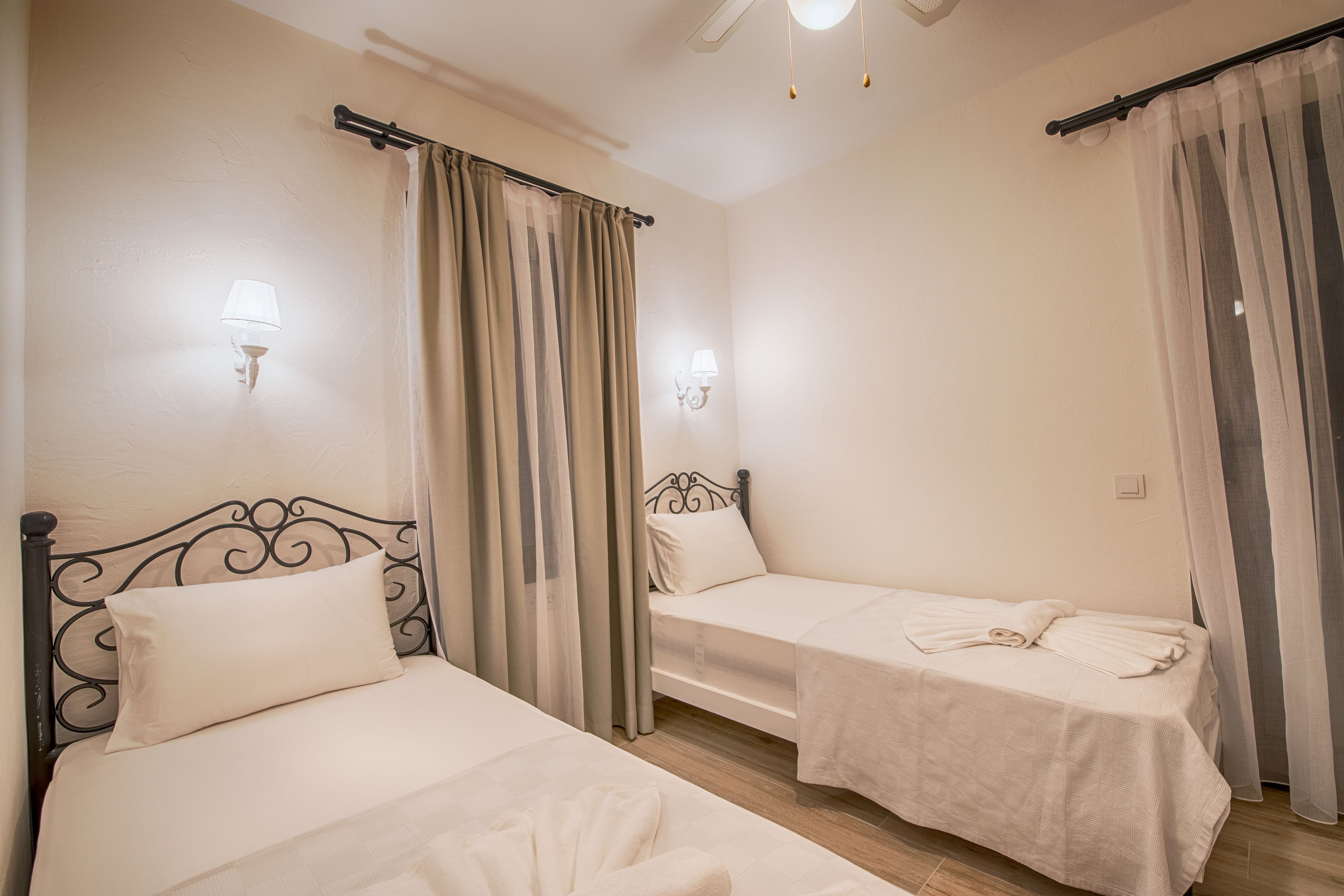 Habitación de hotel con dos camas individuales, cada una con cabecera, mesita de noche y lámpara.