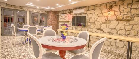A dining area with round tables and chairs, a stone wall, and a TV mounted on the wall.