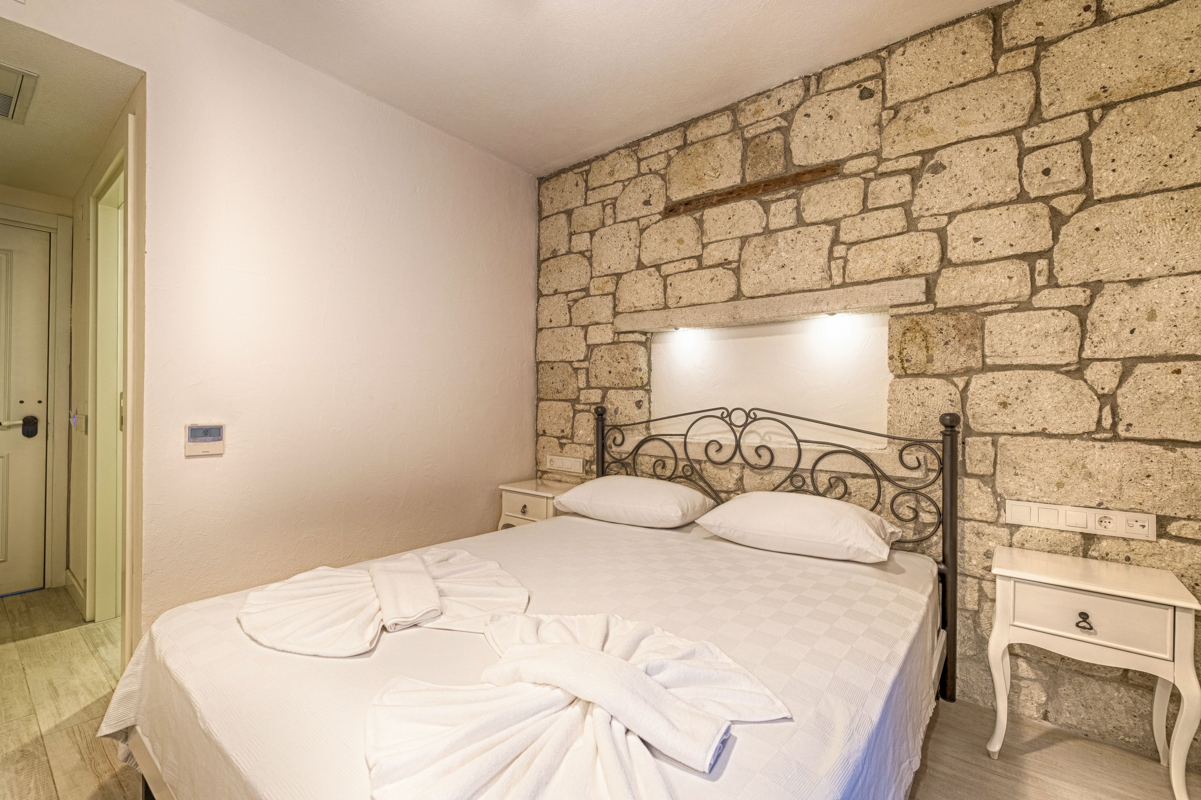 Un dormitorio con pared de piedra, una cama con ropa de cama blanca y una mesita de noche con lámpara.