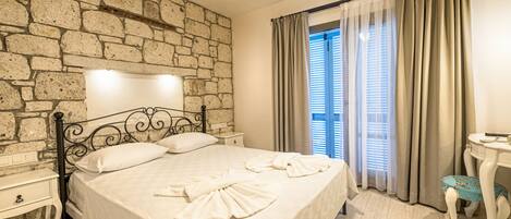A neatly made bed with towels, a stone wall, a nightstand, and a small table with a chair.