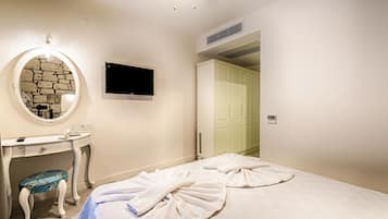 A bedroom with a vanity, a television, and a bed with towels.